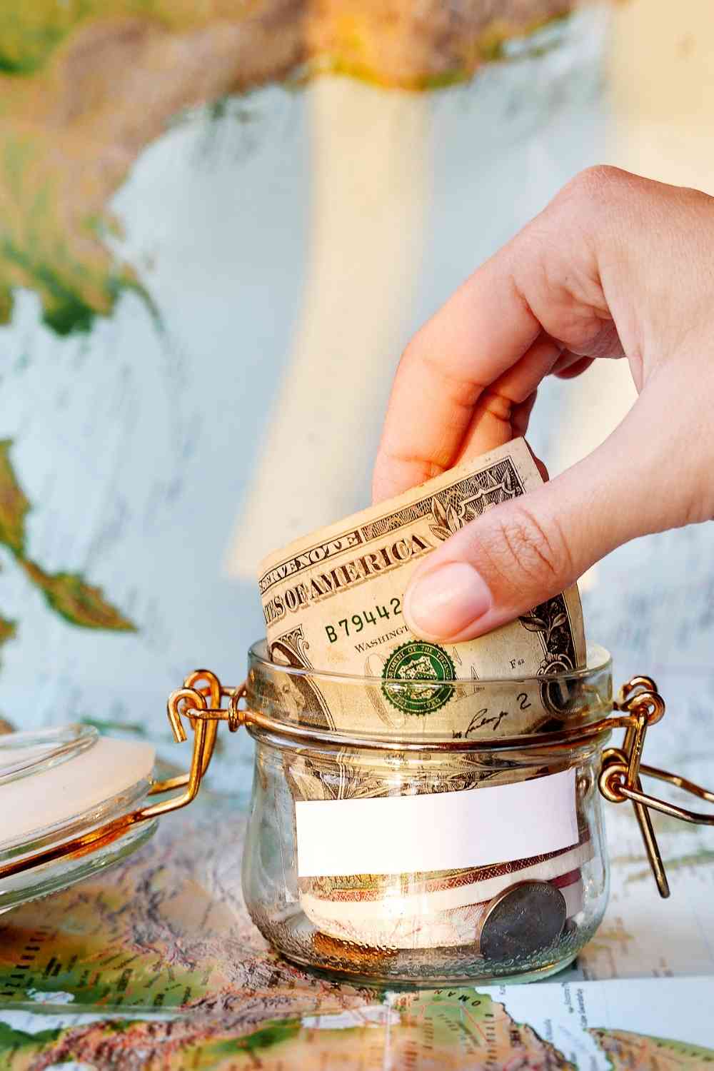 a hand putting in money into a jar to save money for travel