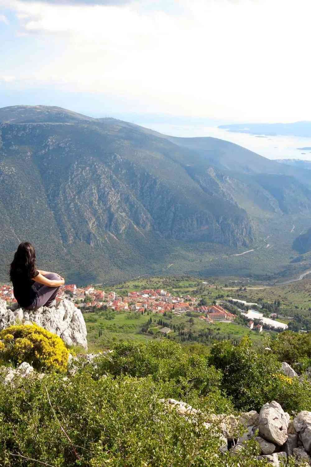 girl sitting on a mountain looking at the small village below