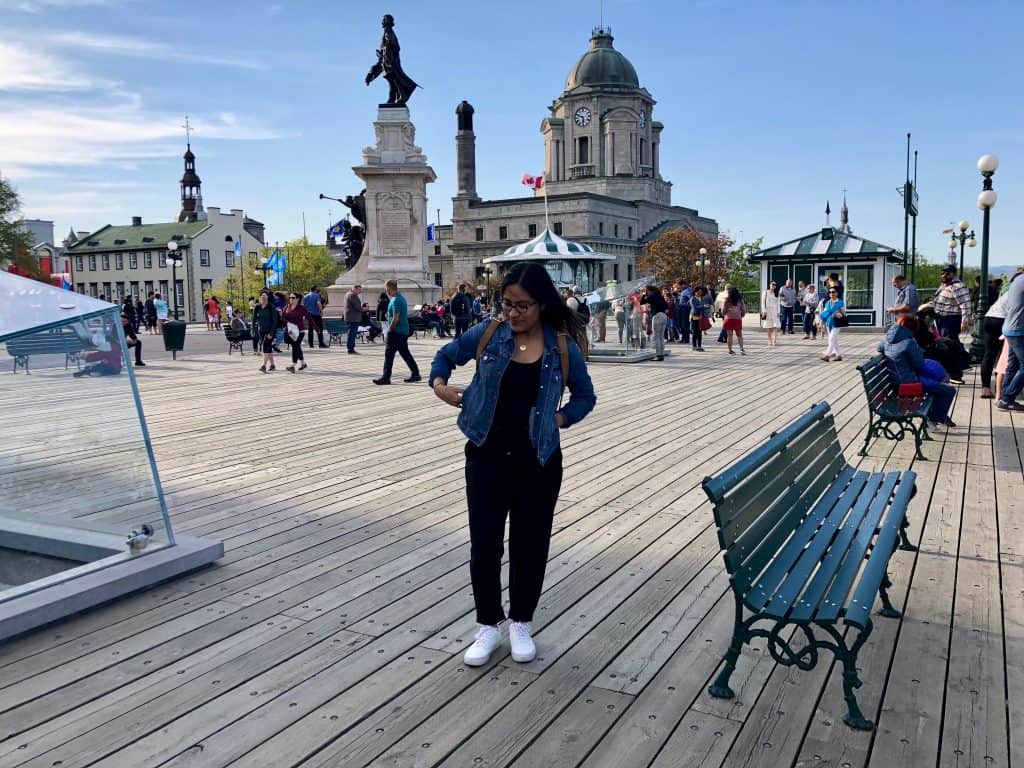 girl with jean jacket, black pants and white shoes standing on boardwalk in quebec city, canada