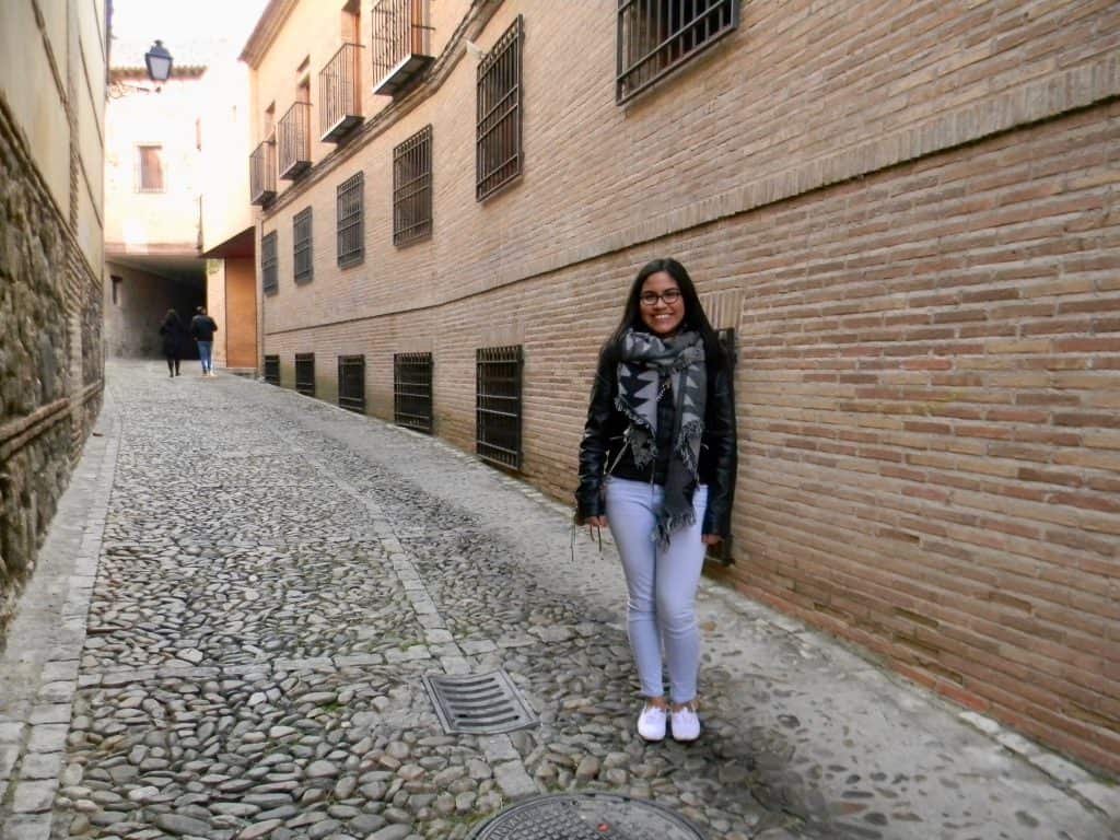 girl in black jacket and light wash jeans posing in a cobble street in a Spanish town Toledo, Spain.