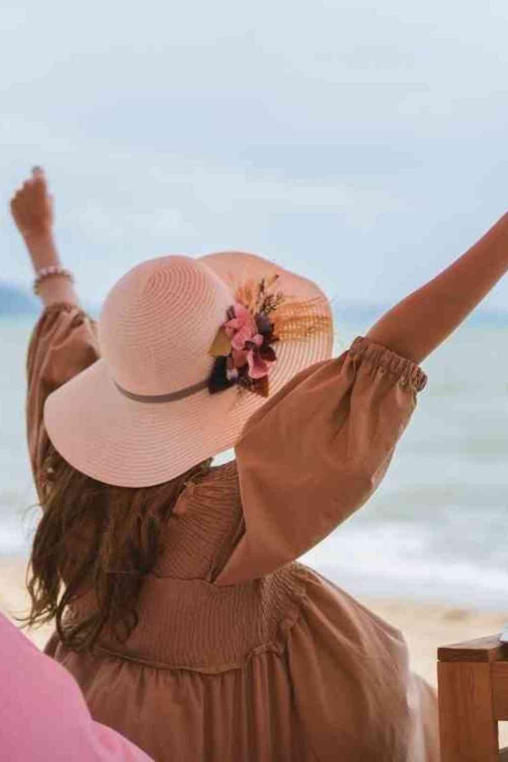 girl with a hat raising her hands up in excitement on the beach