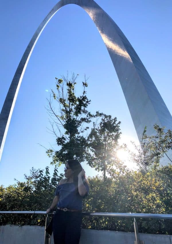 girl standing below the St. Louis Gateway Arch and sunset