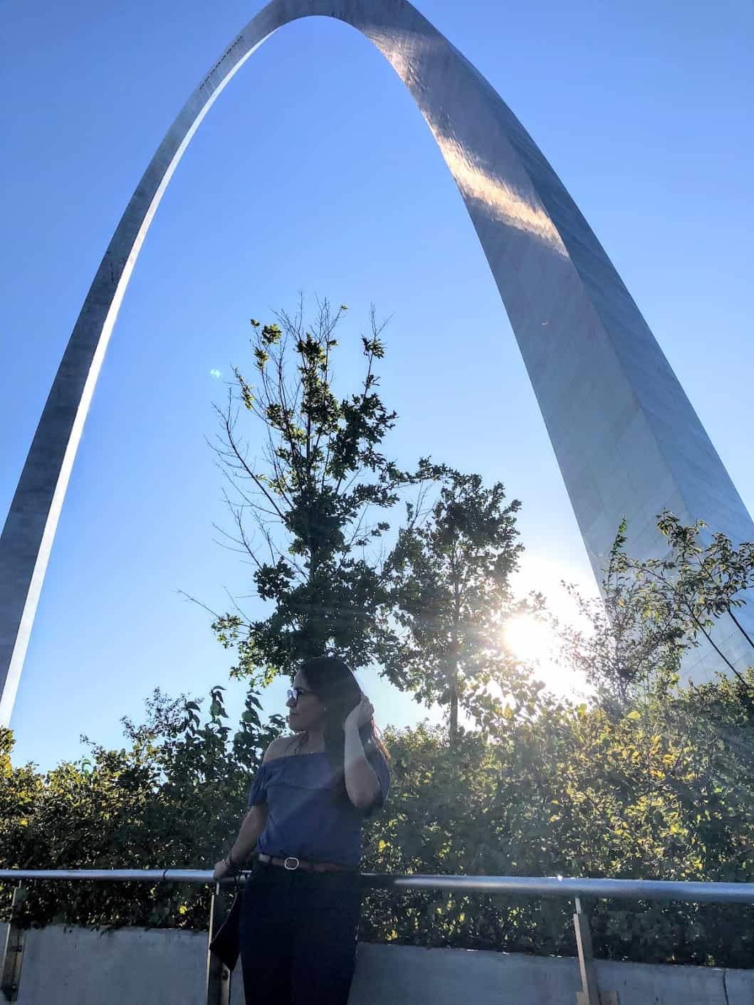 girl standing below the St. Louis Gateway Arch and sunset