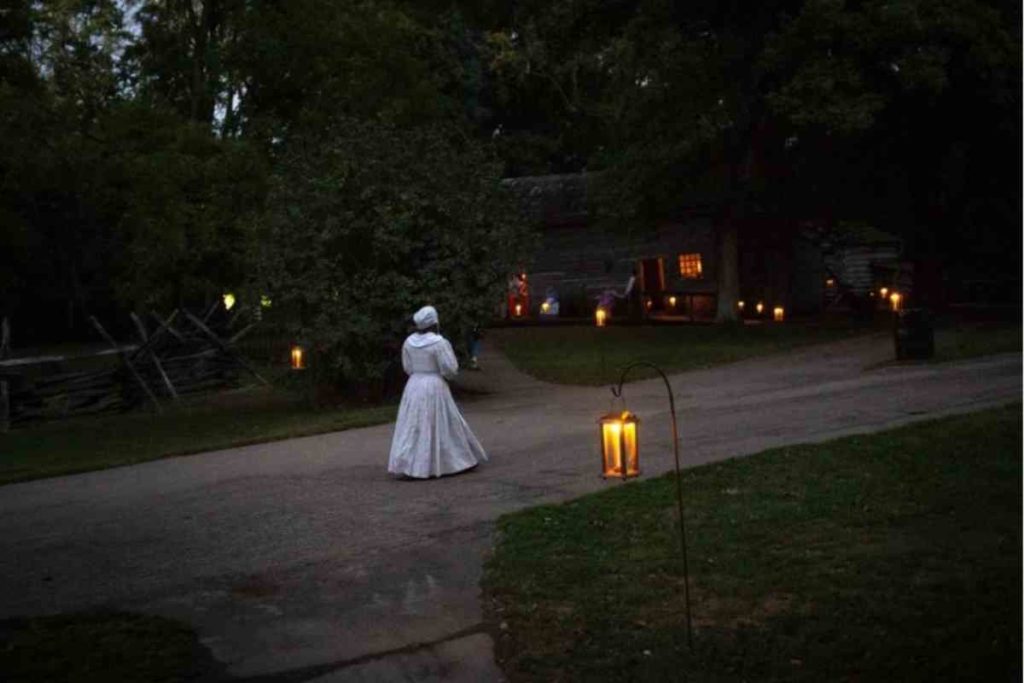 woman walking in a white victorian style dress in a dark road with candles