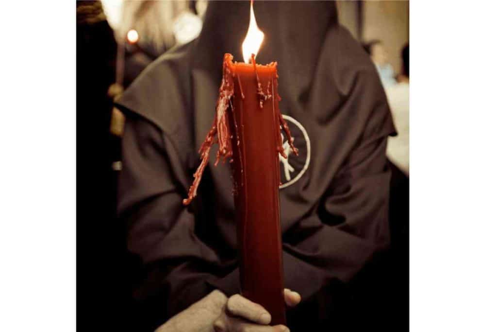 man in religious black gown holding red candle