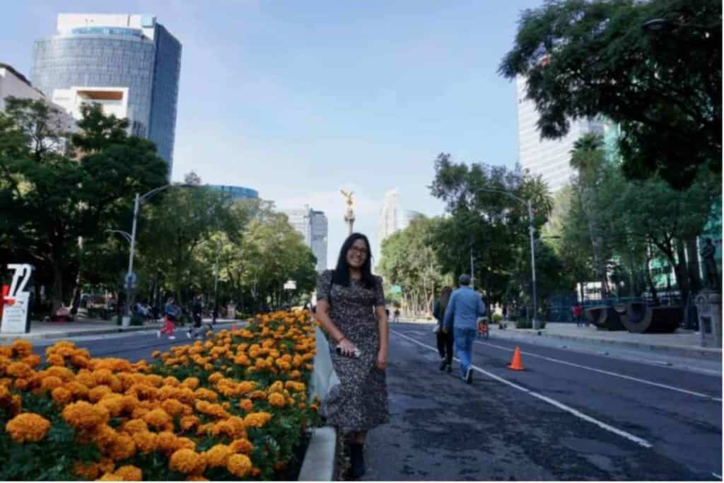Girl with dress standing on Reforma Ave. in front of Angel of Independence with orange flowers