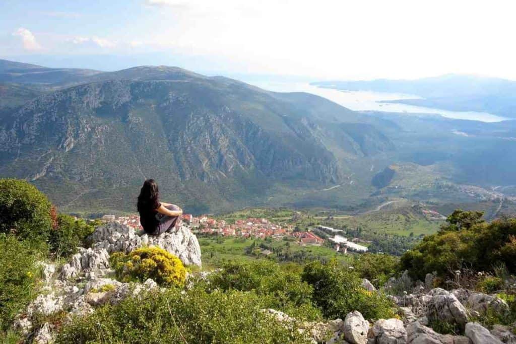 Girl with black shirt and black hair sitting on a rock in the mountains of Delphi, Greece