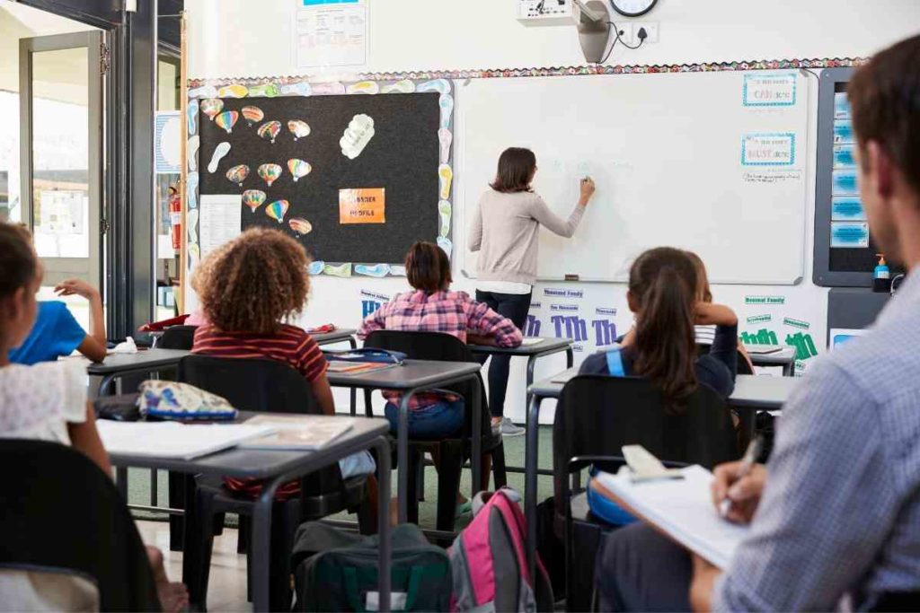 teacher writing on a white board in a class full of students