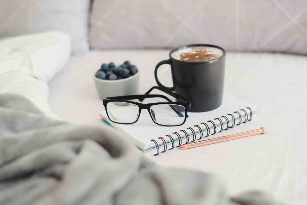 coffee glasses notebook and a cup of blueberries on a bed