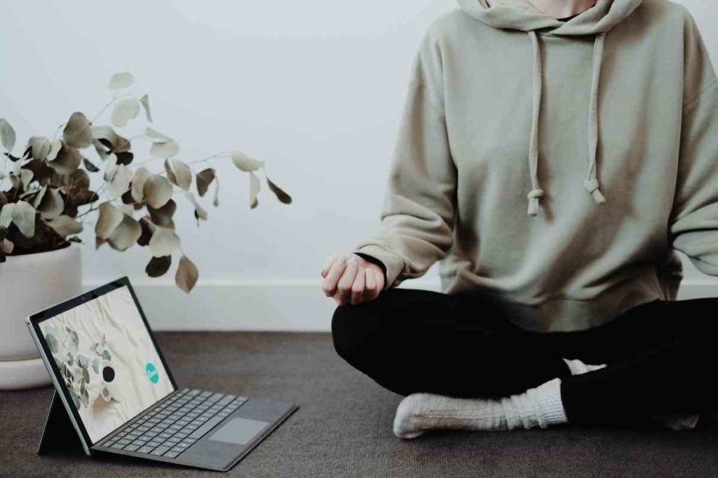 girl with hoodie meditating with computer next to her