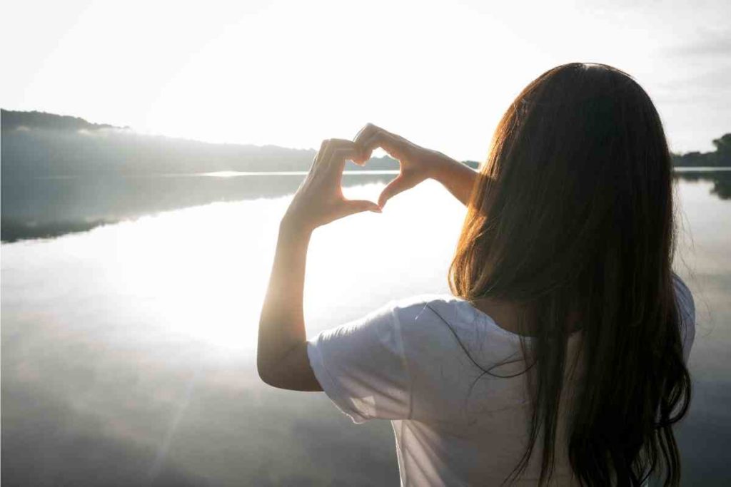 girl making a heart with hands near a lake