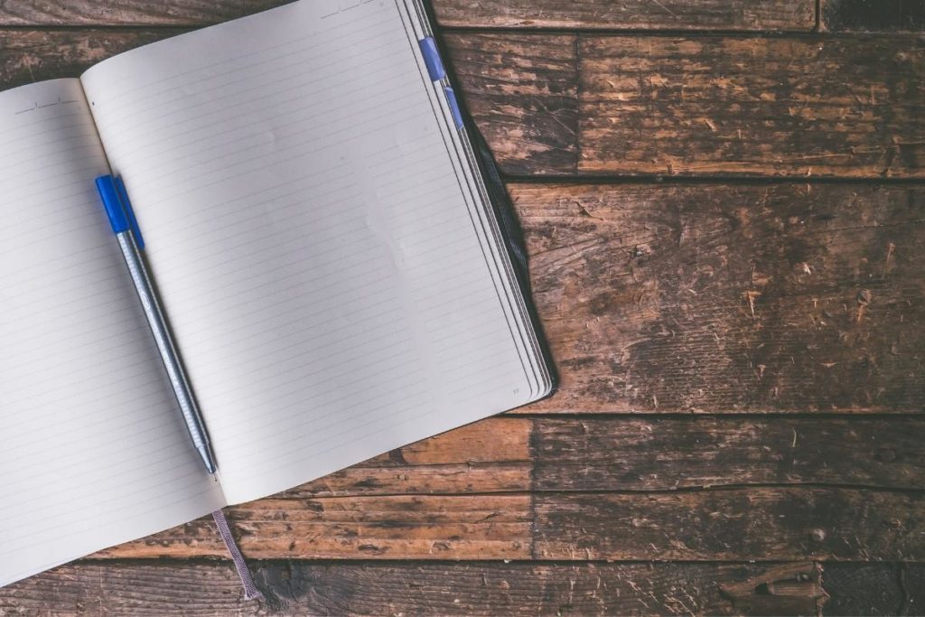 white journal and blank pages on a wooden table with a pen