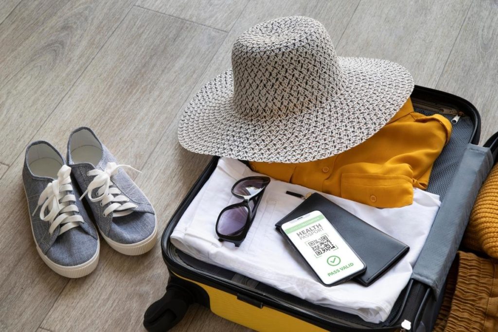 a suitcase full of clothes for travel like a floppy hat orange shirt white jeans and sneakers and sunglasses