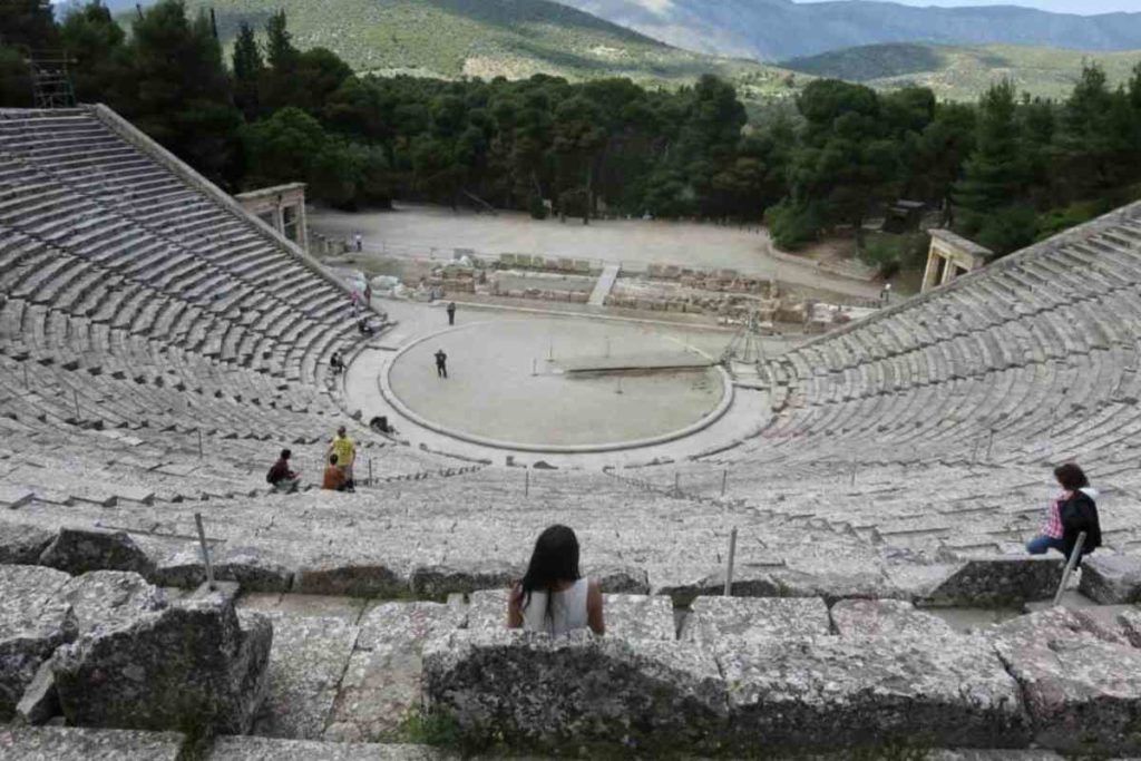 girl sitting in an old greek amphitheater looking into the mountains