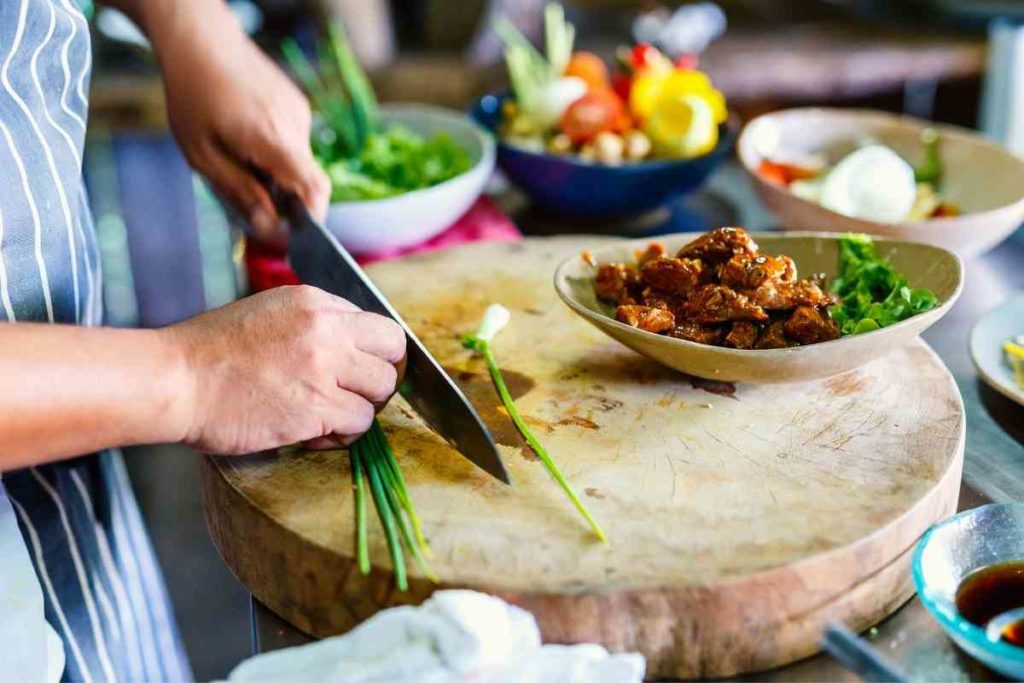 person cutting green onions to put on chicken dish