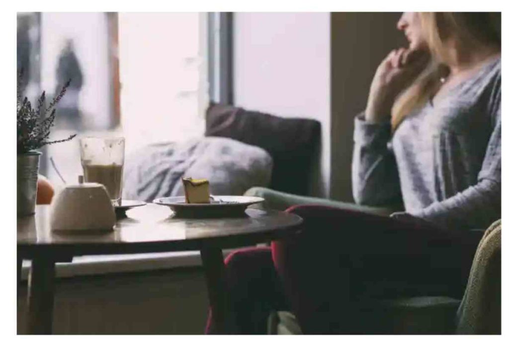 girl sitting on a couch looking out the window on a cloudy day, with a cup of coffee and pastry