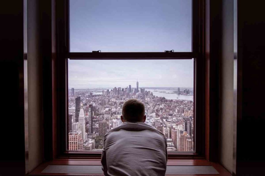 guy leaning outside his window looking out into New York City