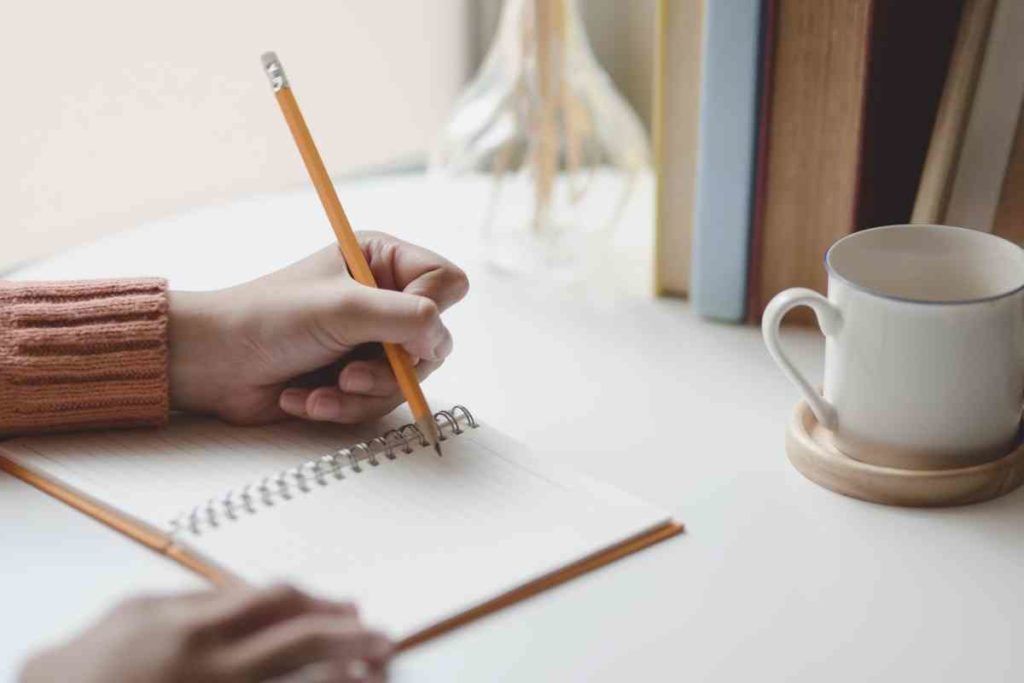 girl writing in her journal with a cup of coffee next to her