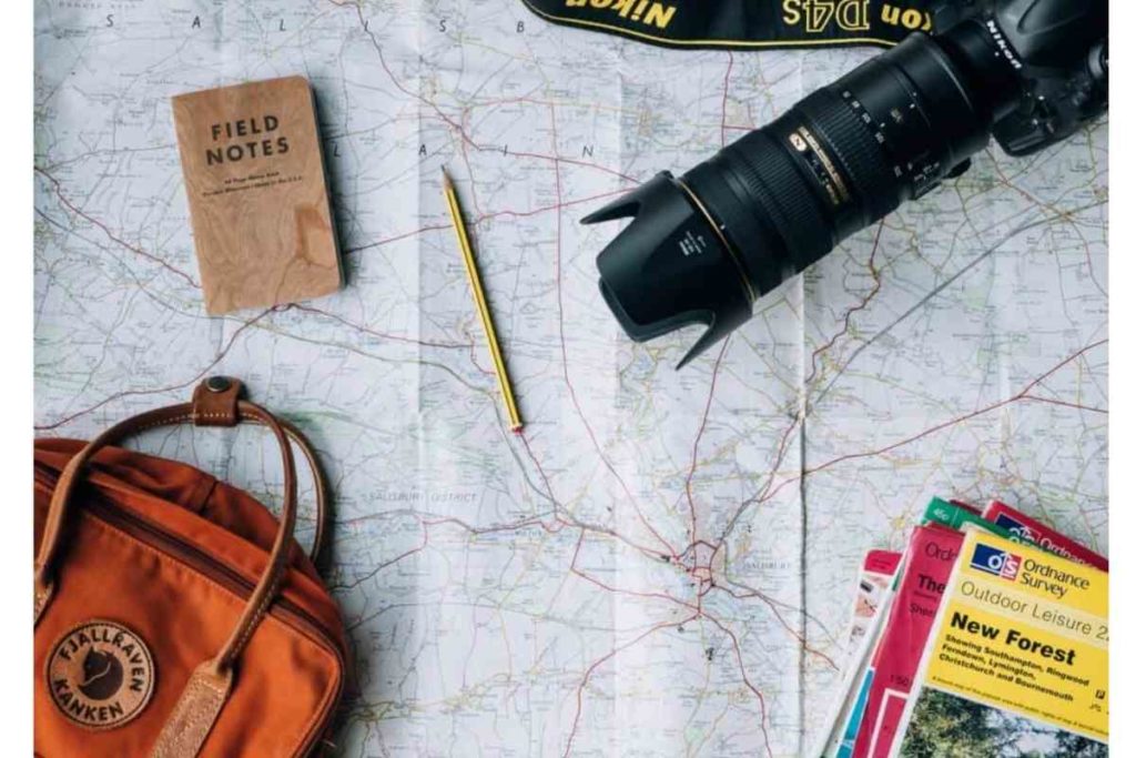 map with a camera travel books notes a pencil and an orange backpack