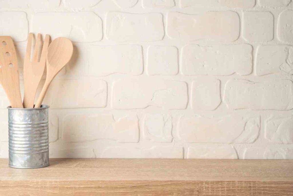 white brick backsplash of a kitchen with wooden counter and tin can with 3 wooden cooking utensils 