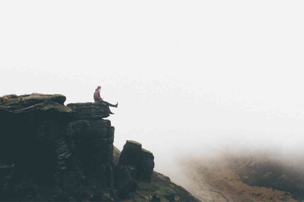 person sitting on the edge of a cliff while traveling alone