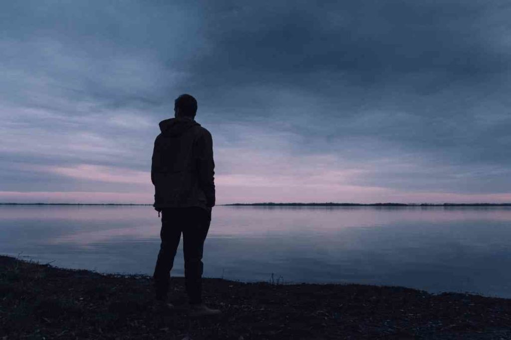 person walking at sunset towards a lake alone