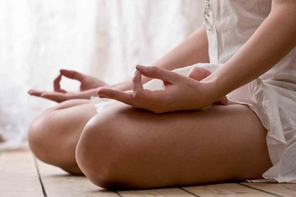 girl sitting down meditating with her fingers in meditation position and resting on her thighs