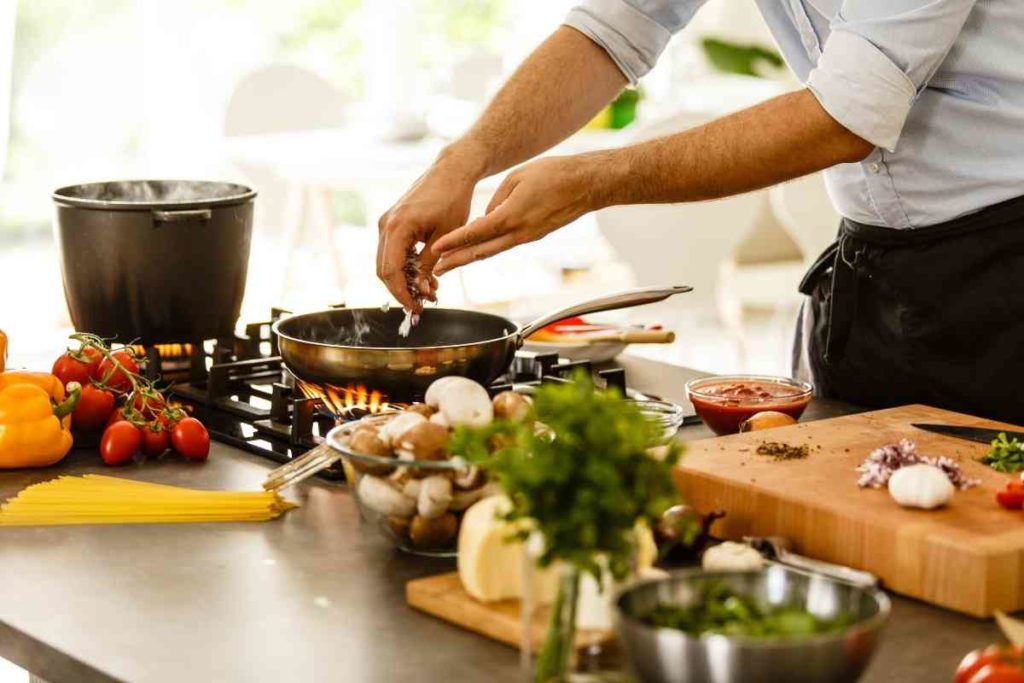 person cooking in their kitchen with fresh vegetables in a pan