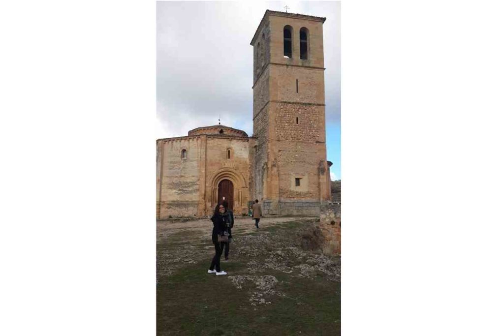 girl with glasses and black coat standing in front of abandoned church in segovia, spain