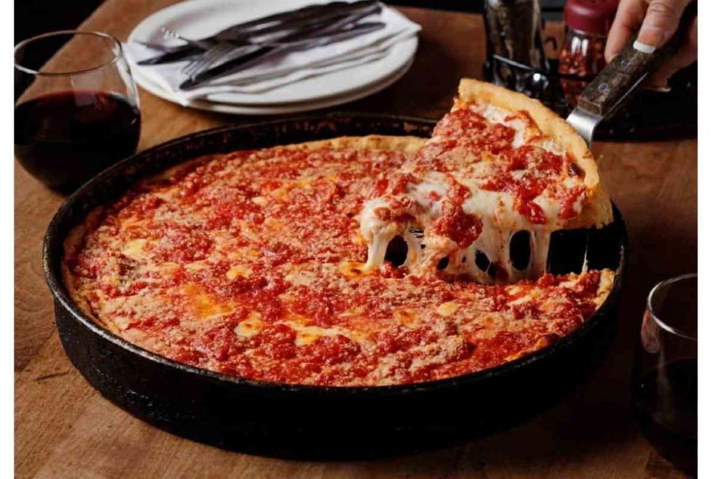close up of Lou Malnati's deep dish pizza with white plates and a glass of red wine