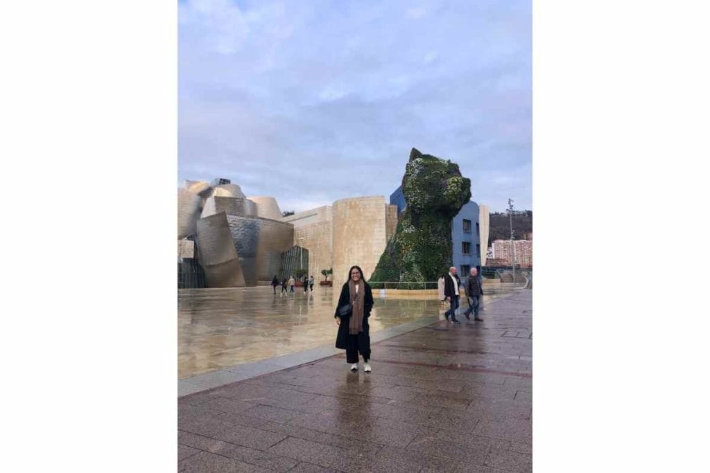 A girl with glasses standing in front of the Puppy and Guggenheim Museum in Bilbao, Spain.