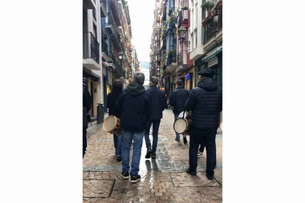 Older Basque men wearing berets and playing instruments as they walk the streets of the historic center of Bilbao