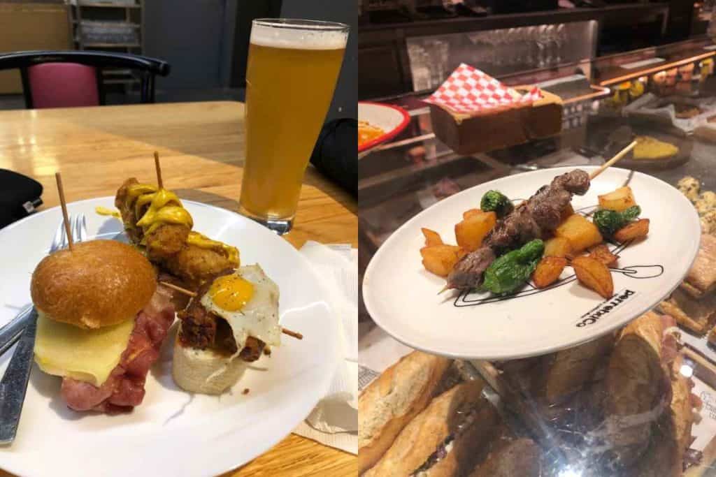 Pintxos in Bilbao consisting of a buger slider with bacon, a fried egg on spanish chorizo on a piece of bread, fried chicken and mustard on a skewer, and a clara con limon drink, and a meat skewer with peppers and padron peppers. 