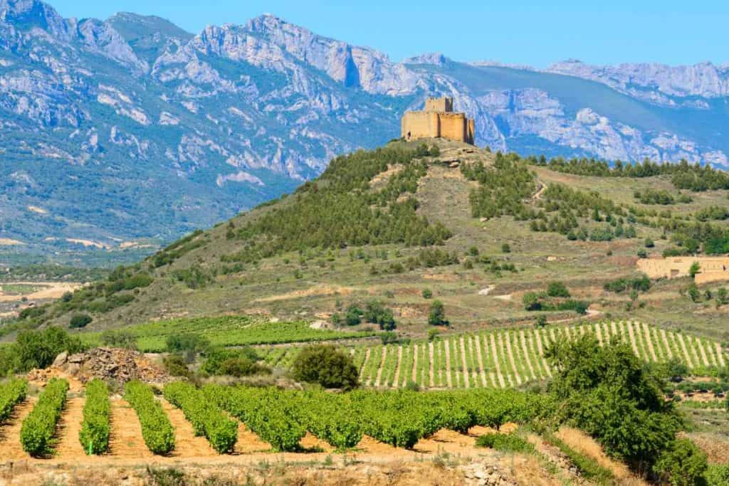 Rolling vineyard hills and a medieval church on top of a hill in La Rioja, Spain.