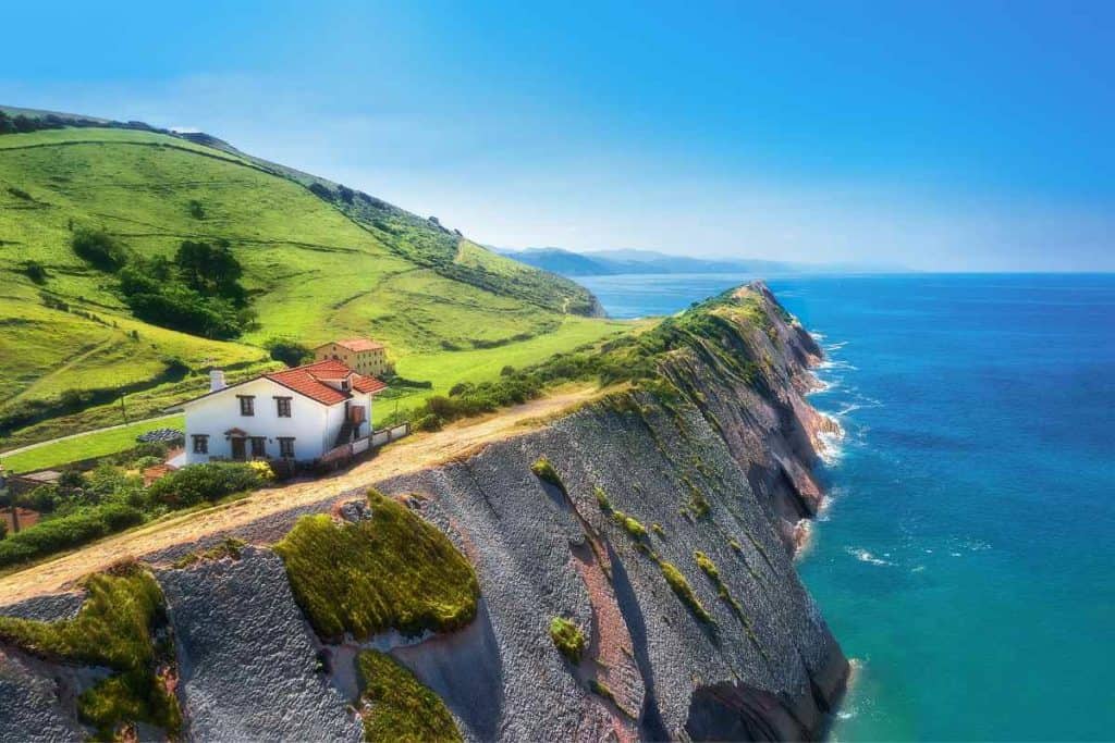 A coastal road by the bay of Biscay, and a white house with a red roof and rolling green hills. 