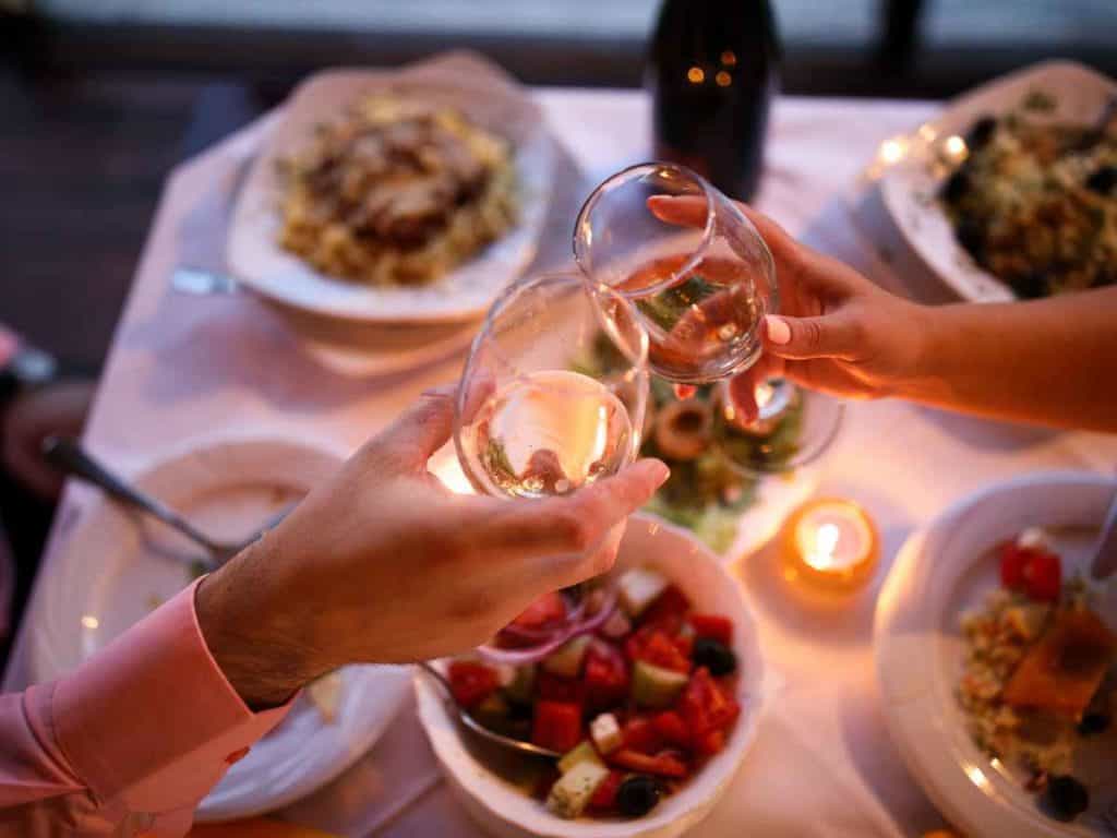 a couple's hand clinking 2 wine glasses over a romantic dinner