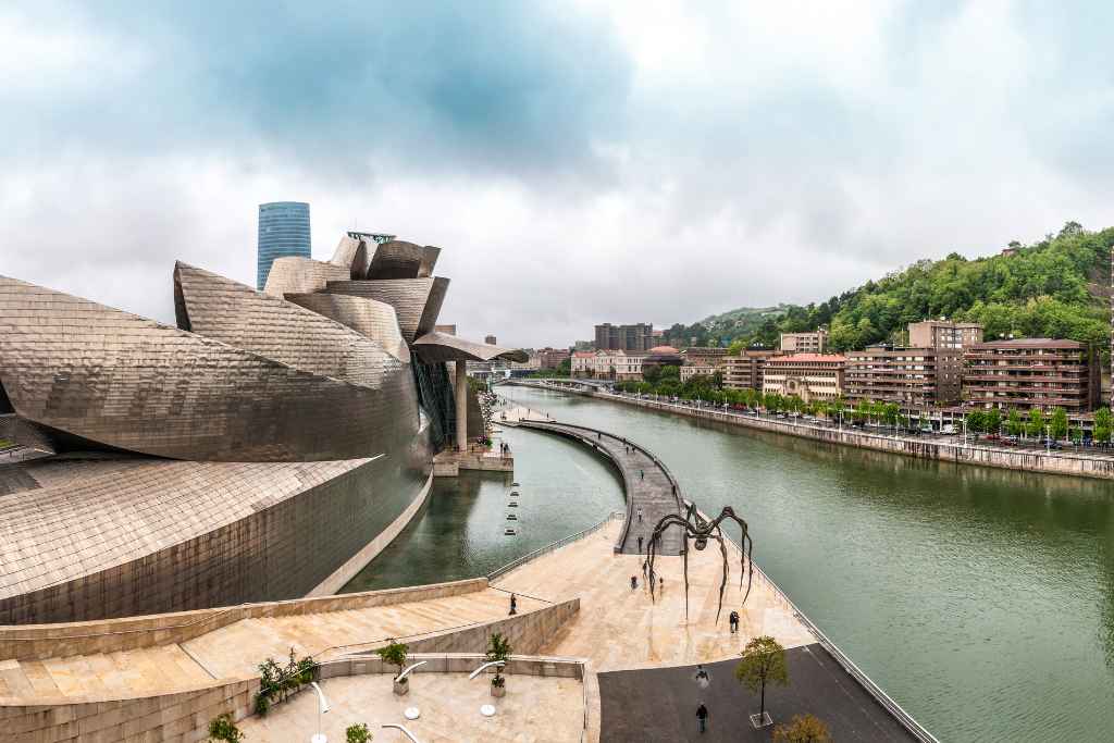 The Guggenheim Museum, a must-see on Bilbao Free Tours, stands as a silver beacon of modern art and architecture, contrasting with the gray skies and green hills.