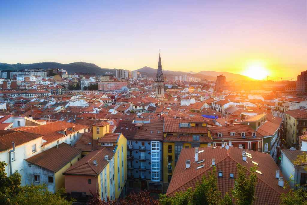 Witness the golden hour on a free tour in Bilbao, with a sunset that drapes the cityscape in warm hues, silhouetting the intricate architecture against the twilight.