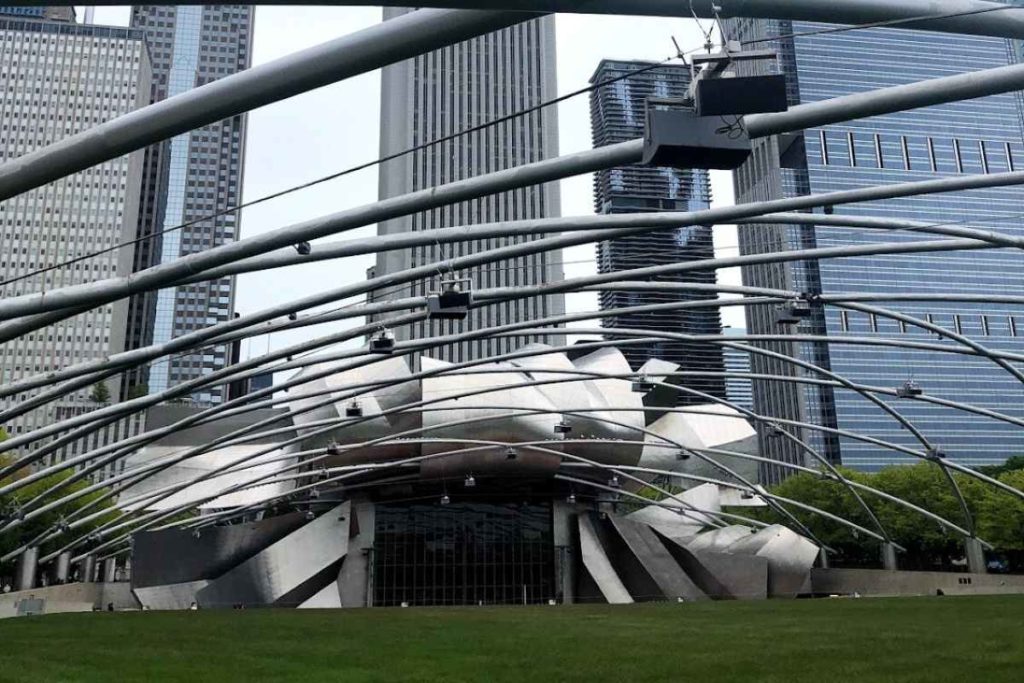 View of the Jay Pritzker Pavilion in Millennium Park, Chicago, featuring its intricate network of stainless steel ribbons that form an avant-garde canopy over the outdoor concert stage. This architectural marvel is set against a backdrop of towering skyscrapers and lush green lawns, offering a dynamic and safe environment for solo travel in Chicago. A perfect blend of urban design and cultural activities, it exemplifies why Chicago is safe for female travelers and highlights engaging things to do in Chicago alone.