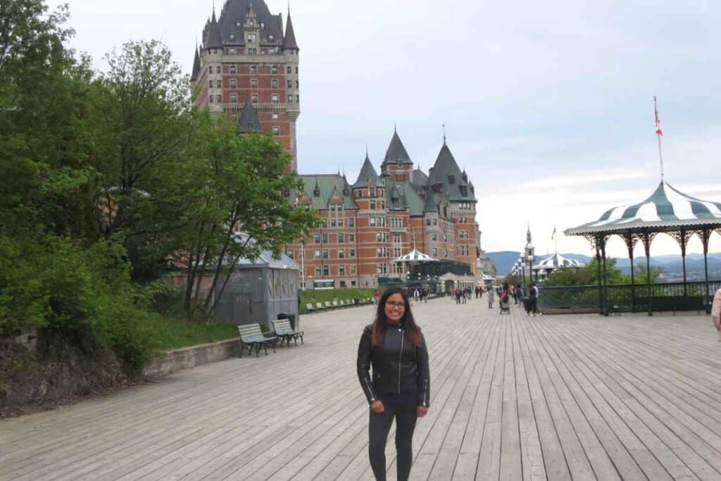 A woman standing on the Dufferin Terrace boardwalk in front of Château Frontenac in Old Québec City, a must-see highlight for first-time visitors.