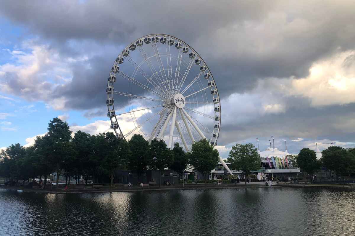 La Grande Roue de Montréal ferris wheel stands tall against a moody sky, reflecting off the water in the Old Port at sunset.