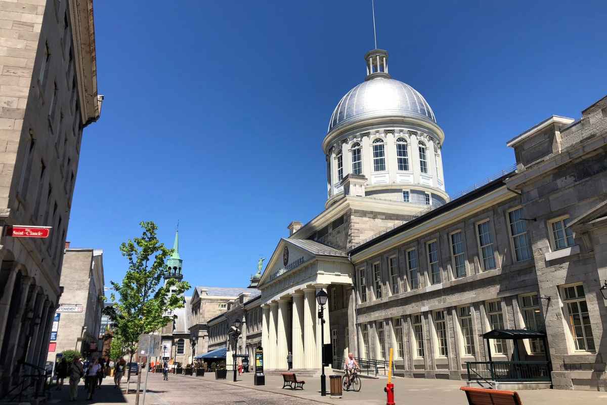 The silver dome of Marché Bonsecours rises over a cobblestone pedestrian street in Old Montréal on a bright summer day.